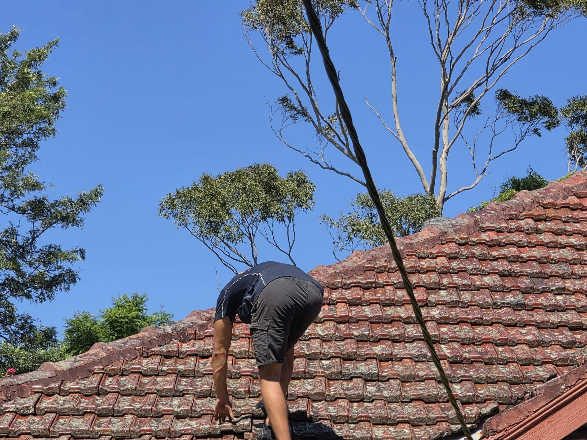 Crown Roofers technician inspecting terracotta tile roof Sydney blue sky